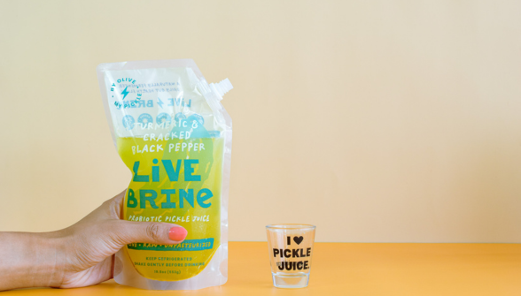 Person holding Live Brine juice product with I Love Pickle Juice label on yellow background