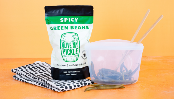 Spicy green beans in a clear bag, a jar of pickles, a bowl of pickles